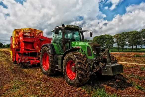 Grüner Traktor mit einem roten Anhänger steht auf einem Feld - In diesem Beitrag erfahren Sie wissenswerte Infos darüber, wie aus Traktoren High-End Technologie-Maschinen wurden.